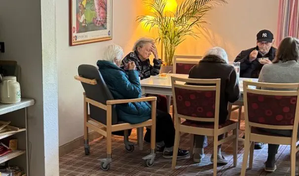Bewohner der Demenz-WG sitzen gemeinsam am Tisch beim Essen – gemütlicher Gemeinschaftsbereich mit warmem Licht © Foto: Hambückers